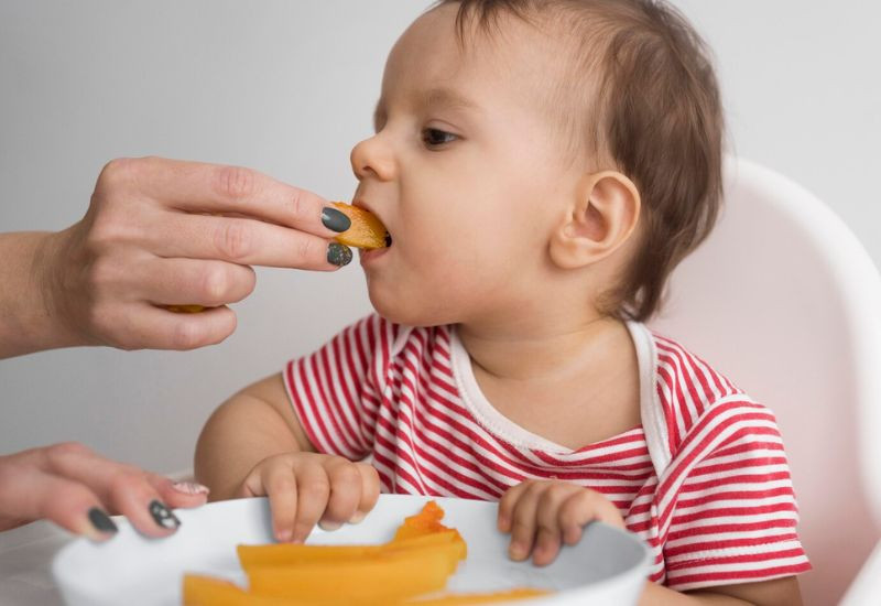 Một em bé đang chơi đồ chơi trong khi bác sĩ kiểm tra sức khỏe, minh họa tầm quan trọng của việc xét nghiệm vi chất cho bé.